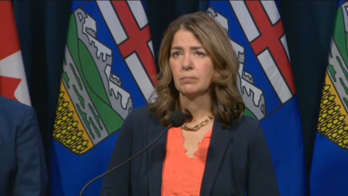 Premier Danielle Smith stands at a podium, in front of flags.