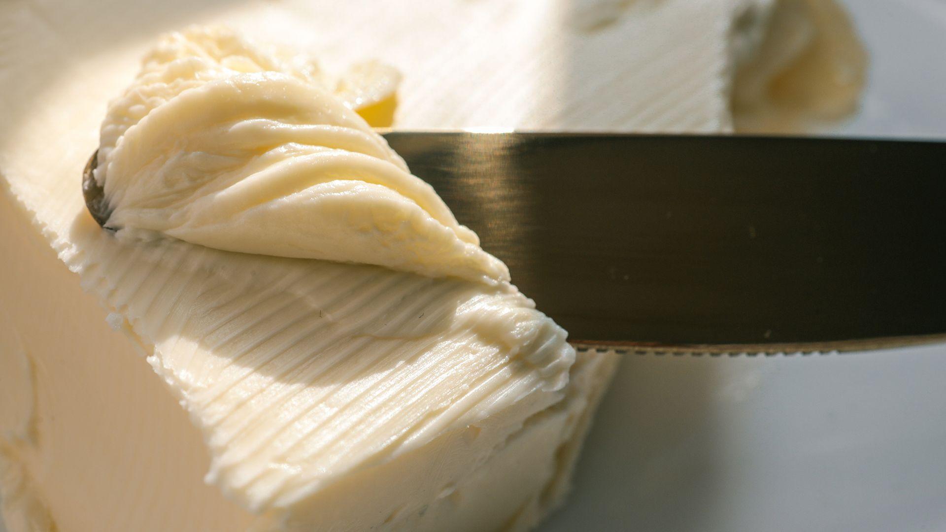Stock photo shows a close up image of a knife running through margarine with a spot of sunlight pouring in.