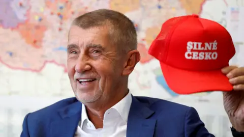 Reuters Andrej Babis stands in front of a map of the US holding a red cap saying Silné Česko meaning 'Strong Czechia'
