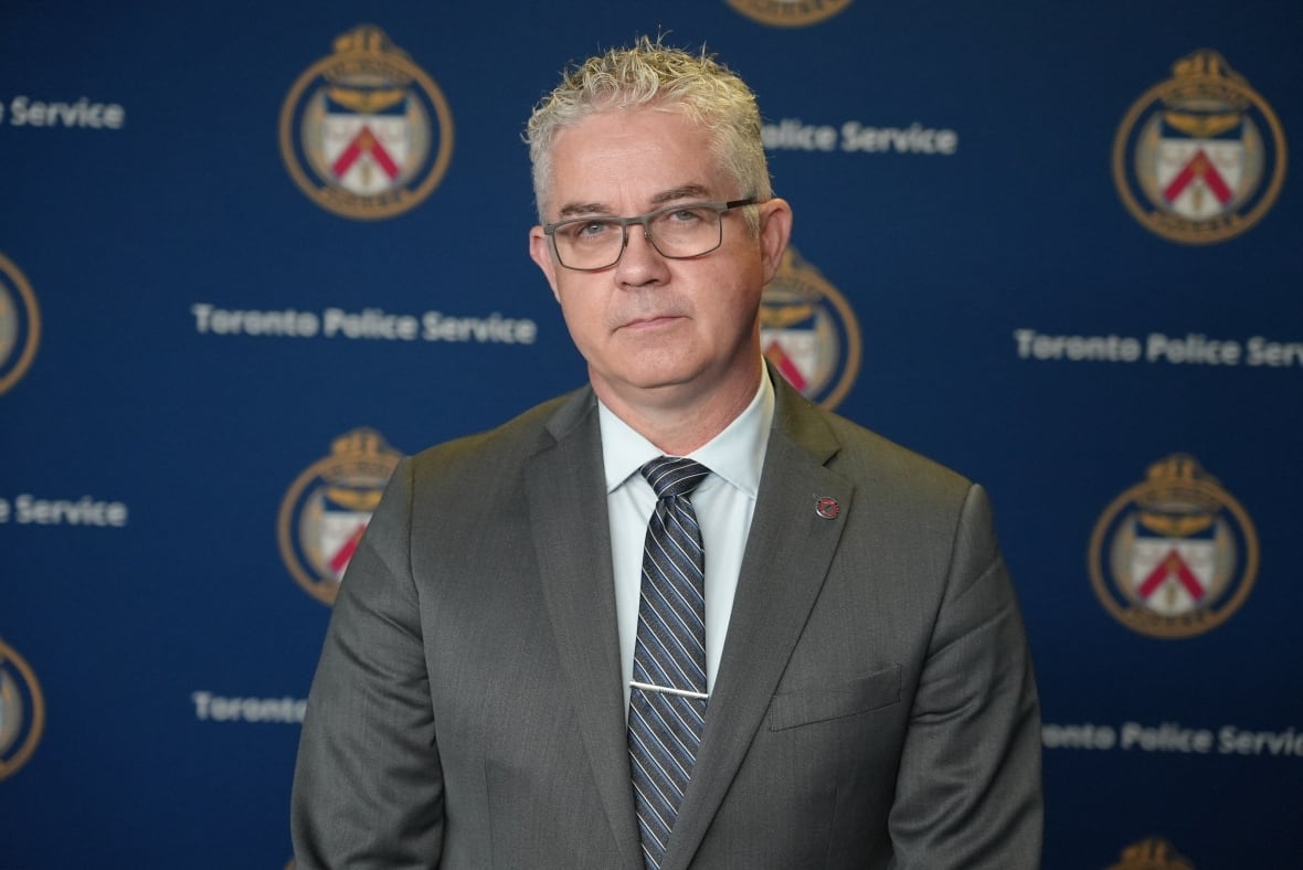 Man in a suit standing in front of a wall with Toronto police logos on it.