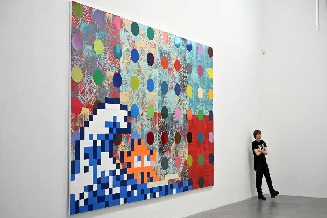 A gallery assistant stands next to the artwork 'Troubled Waters', 2025, by US artist Shepard Fairey, British artist Damien Hirst, and French street artist Invader during an exhibition photo call at Newport Street Gallery, London on October 9, 2025. The exhibition of individual and collaborations by US artist Shepard Fairey, British artist Damien Hirst, and French street artist Invader entitled 'Triple Trouble' will run from October 10 to March 29, 2026. (Photo by Justin TALLIS / AFP) / RESTRICTED TO EDITORIAL USE - MANDATORY MENTION OF THE ARTIST UPON PUBLICATION - TO ILLUSTRATE THE EVENT AS SPECIFIED IN THE CAPTION