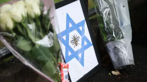 EPA A framed Star of David with a bee, the symbol of Manchester, is left at the scene of a deadly terror attack in Manchester. Bunches of lowers have also been left on either side of the picture. 