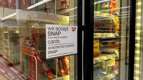 Universal Images Group via Getty Images A sign on a grocery store fridge reads "We accepts SNAP food stamp program' in both English and Spanish. Frozen food is seen in the background. 