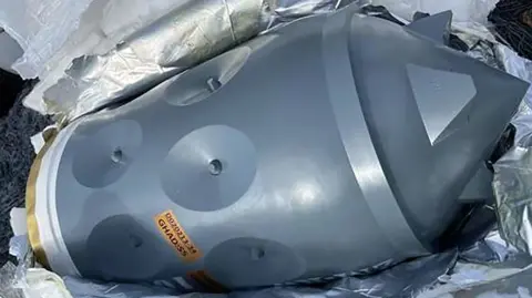 US Department of Justice A close-up photo of a silver Iranian-made warhead. It appears to be lying on its side and surrounded by shiny silver packaging.
