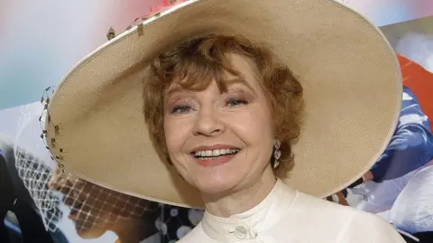 Getty Images Prunella Scales is shown in middle age wearing a prominent wide-brimmed hat and smiling.