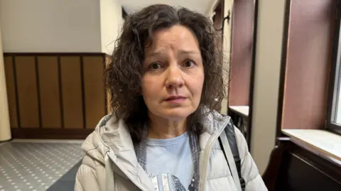 BBC/Sarah Rainsford A woman with dark curly hair and a beige coat looks at the camera
