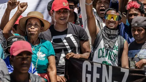 AFP via Getty Images Residents and protesters cheer and hold banners as they gather for a civil society rally outside City Hall in Antananarivo, on Monday.
