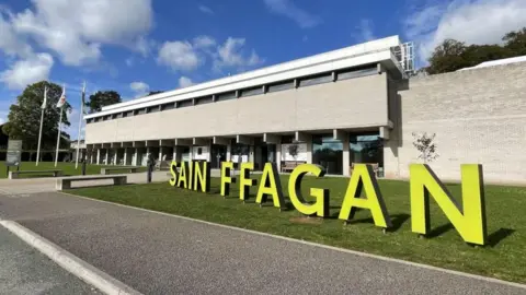 BBC The exterior of museum with large yellow letters individually standing which spell out "SAIN FFAGAN" in capitals.
