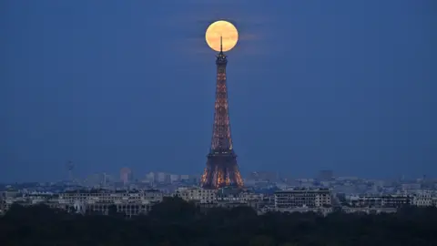 Anadolu via Getty Images The bright supermoon sitting at the tip of the Eiffel Tower in Paris