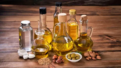 Getty Images Assorted healthy vegetable oil bottle collection on wooden table in a old fashioned kitchen with low key illumination: Olive oil, hazelnut oil, almond oil, coconut oil and sesame oil