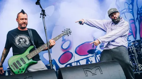 Stefan Hoederath/Redferns via Getty Images Rivers has a mohawk and a bright green bass guitar and Fred Durst has a grey beard and purple jumper on.