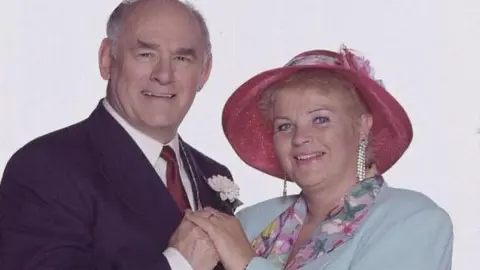 BBC The actor Tony Caunter playing Roy Evans in a smart wedding suit next to Pam St Clement as Pat Butcher at their wedding in EastEnders 