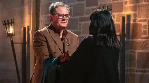 Alan Carr receiving his Traitors cloak from Claudia Winkleman