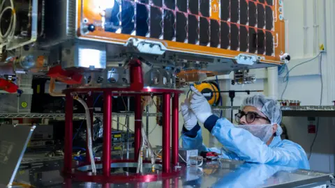 UK MoD A man wearing protective gear fixes the Tyche satellite in a laboratory.

