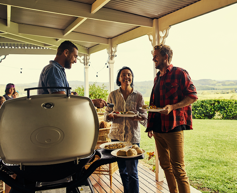 people standing around a gas barbeque having a good time.