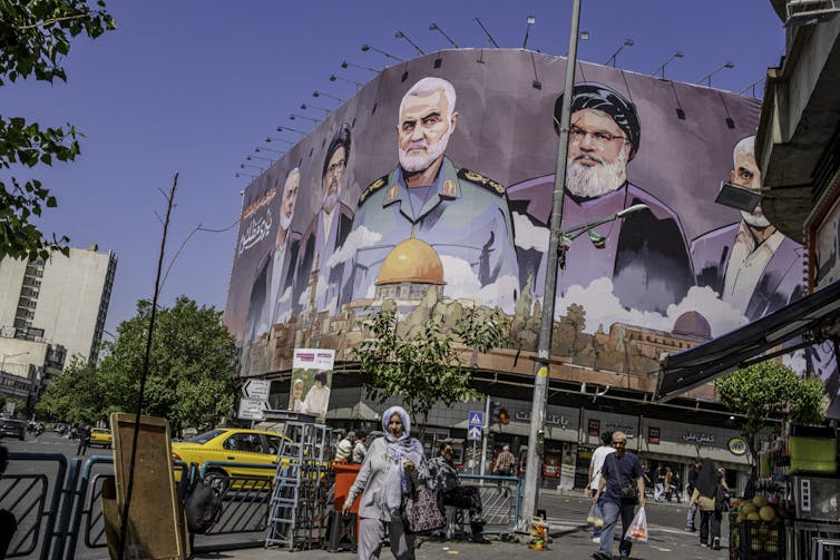 people walk on street past large billboard depicting slain anti-israel leaders