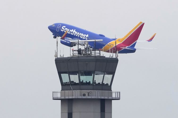 a colorful plane flies near the top of an air traffic control tower