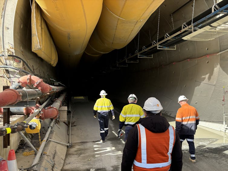 tunnel for hydro project, workers in hard hats walking through it.
