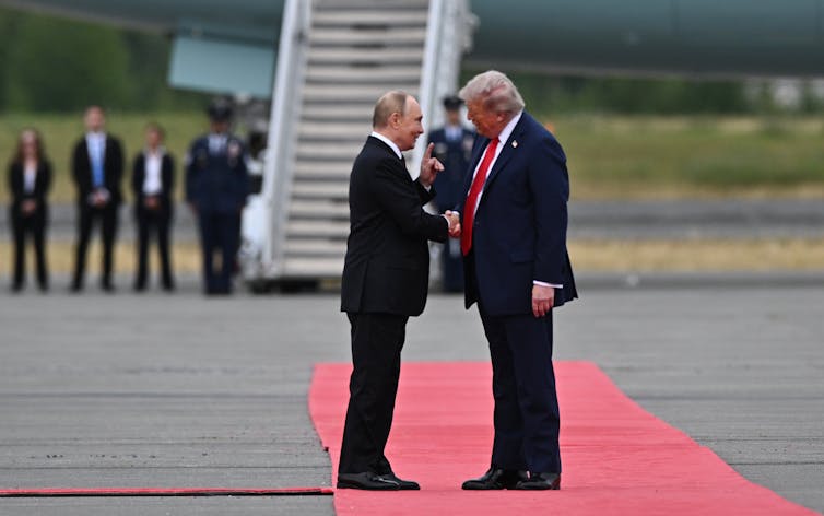 Trump and Putin greet each other on a red carpet.