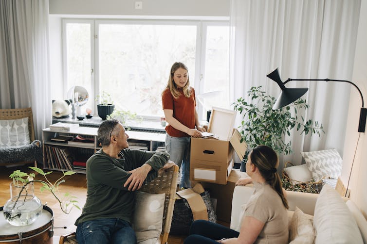 A young woman unpacks a moving box while talking to her parents.