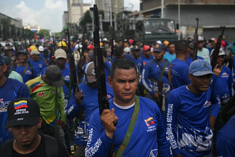 Men and women in blue tops hold guns and march.