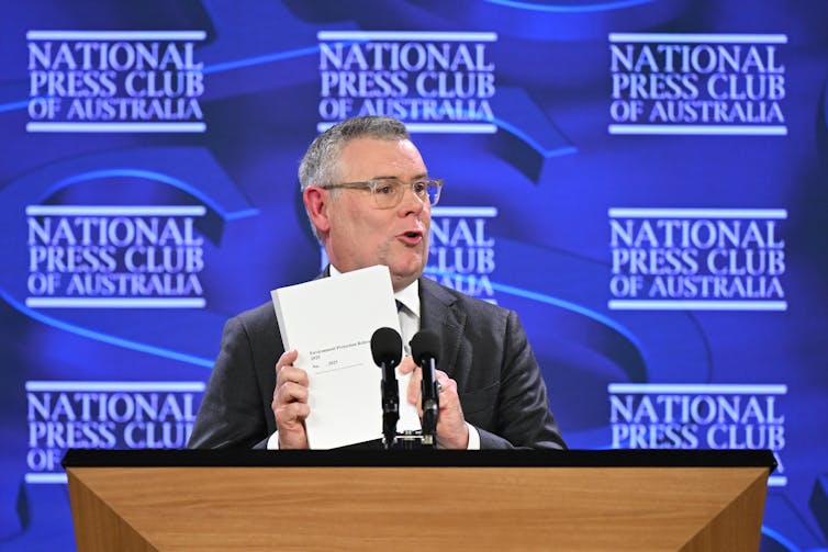 man holding paper at press club event.