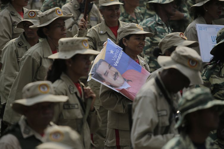 People in fatigues stand around, one holding a poster.