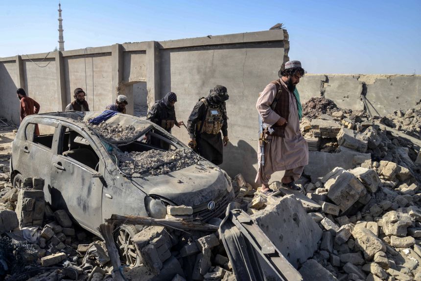 Taliban security personnel walk past a damaged car in the Spin Boldak district of Kandahar province on October 16, 2025, a day after the cross-border clashes between Afghanistan and Pakistan.