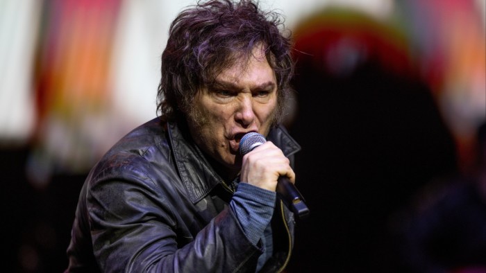 Javier Milei sings into a microphone on stage during the presentation of his book 'La Construccion del Milagro'.