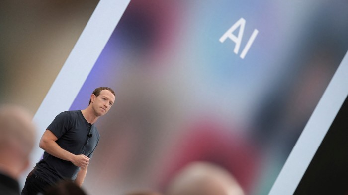 Mark Zuckerberg speaks on stage with the letters ‘AI’ displayed on a large screen behind him.
