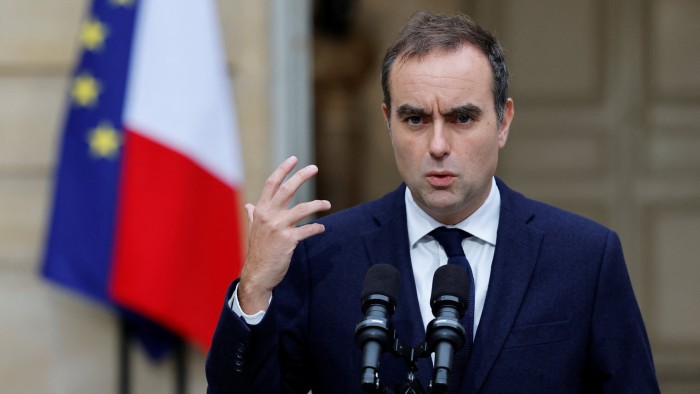 Sebastien Lecornu gestures while speaking at microphones, with the French and EU flags visible in the background.