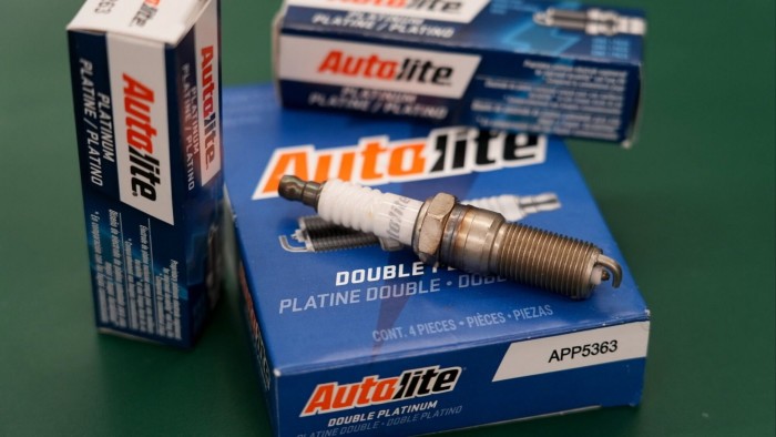 Autolite spark plug resting on a blue Autolite Double Platinum box, with additional Autolite spark plug boxes in the background.