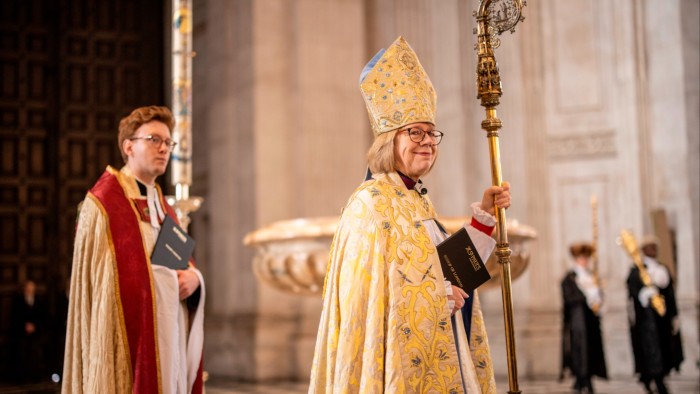 Dame Sarah Mullally, dressed in ceremonial vestments and holding a staff, stands inside a cathedral.