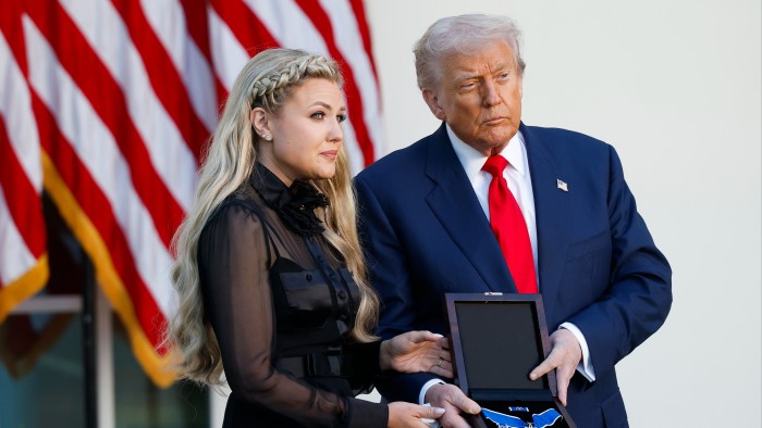 Donald Trump presents the Presidential Medal of Freedom in a box to Erika Kirk, with American flags in the background.