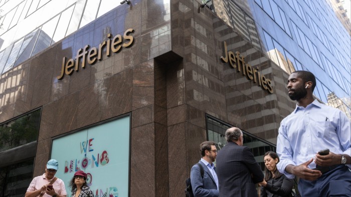 People stand and walk outside the Jefferies headquarters in New York, with the company name displayed on the building