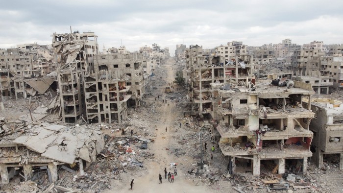 Several people walk among the ruins of heavily damaged buildings in Gaza City after the withdrawal of Israeli forces.