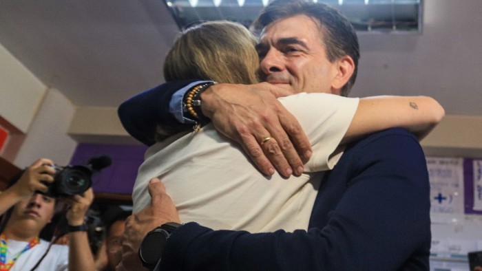 Rodrigo Paz embraces a supporter at a polling station, with a photographer capturing the moment in the background.