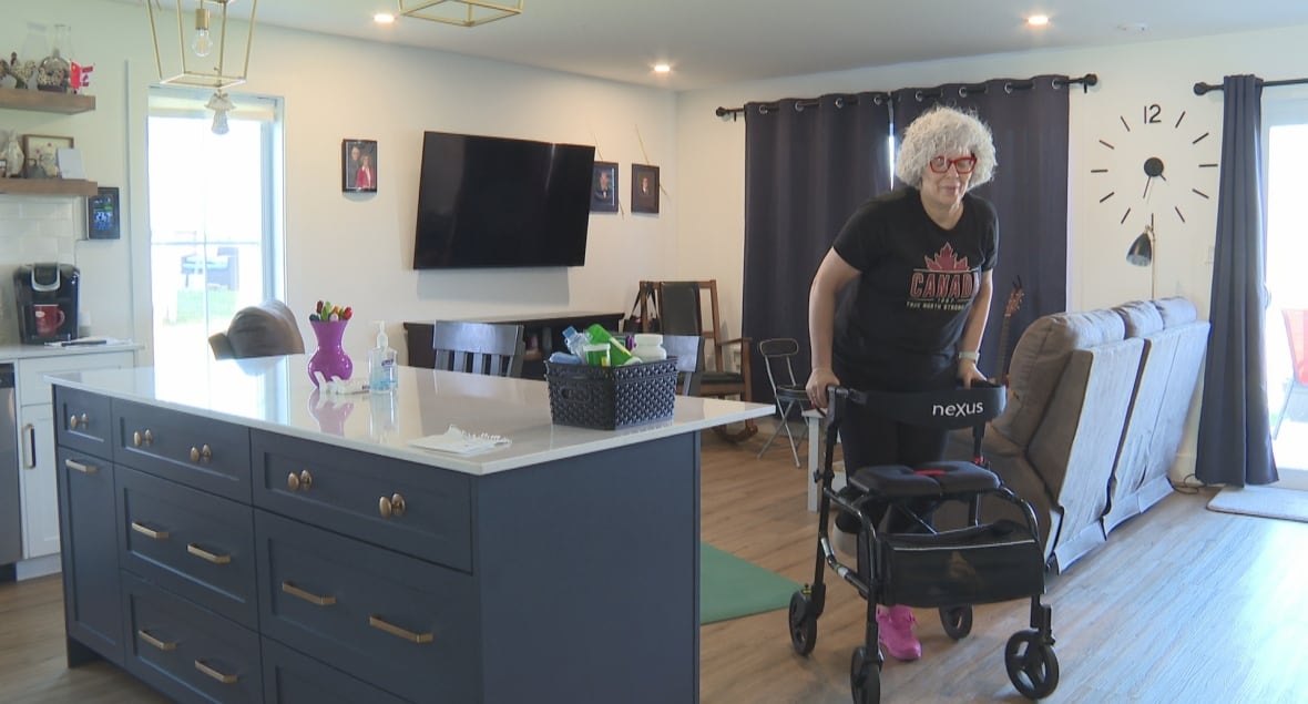 A woman in a black T-shirt uses a walker to pass through a living room. 