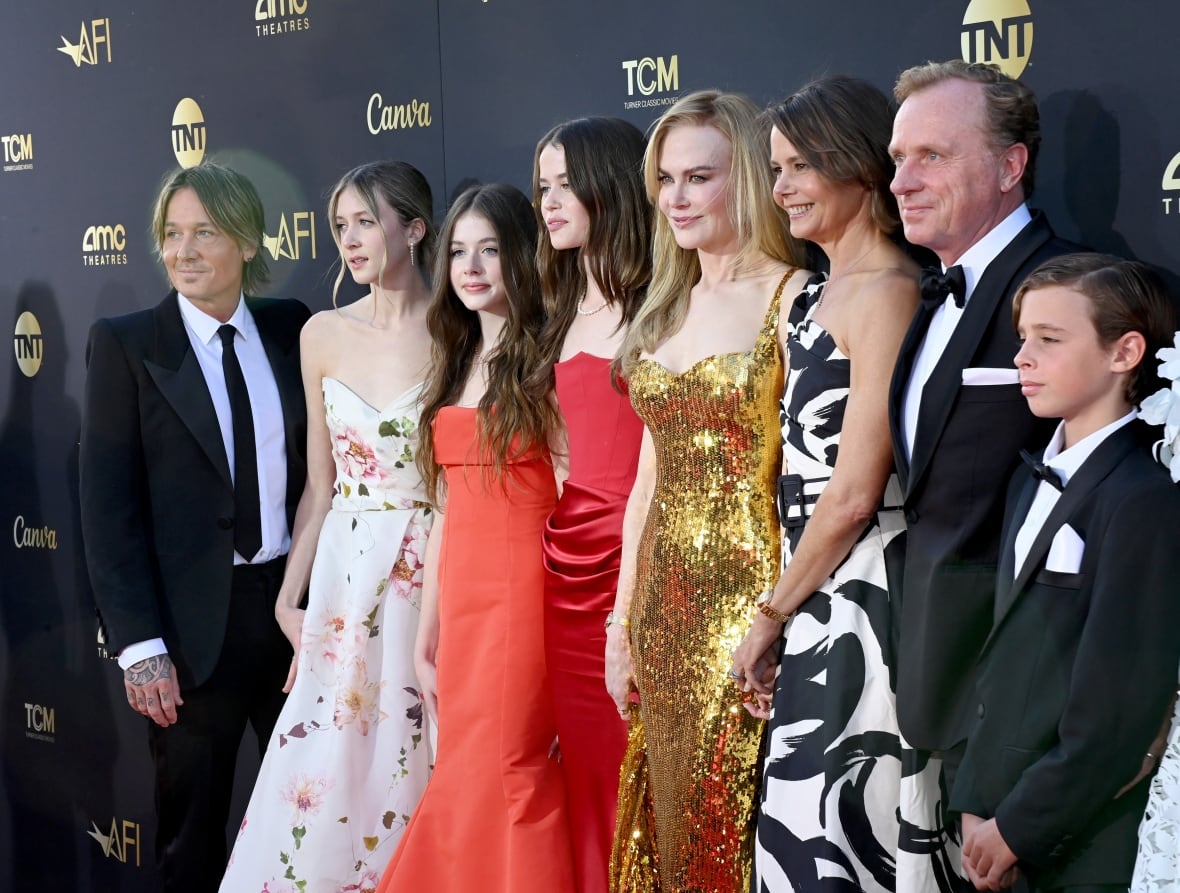  A family in formal wear, men and boys in black suits and ties and women and girls in gowns, pose for a photo in front of a black backdrop. 