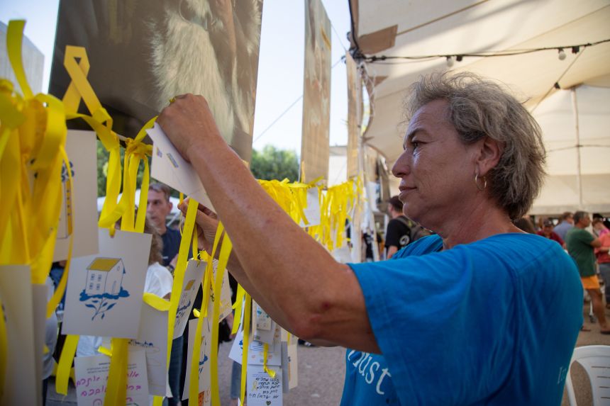 A woman ties a yellow ribbon and a card for the hostages at a tent in Tel Aviv's Hostages Square.