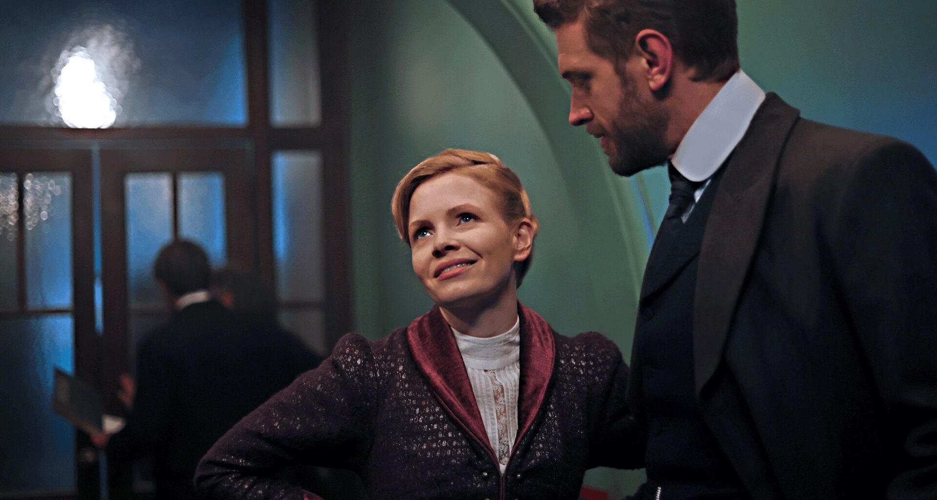 A color image from the set of Miss Scarlet Season 6 showing actor Kate Phillips in costume as Eliza Scarlet next to actor Tom Durant-Pritchard as DI Alexander Blake. The period mystery series airs on MASTERPIECE on PBS.