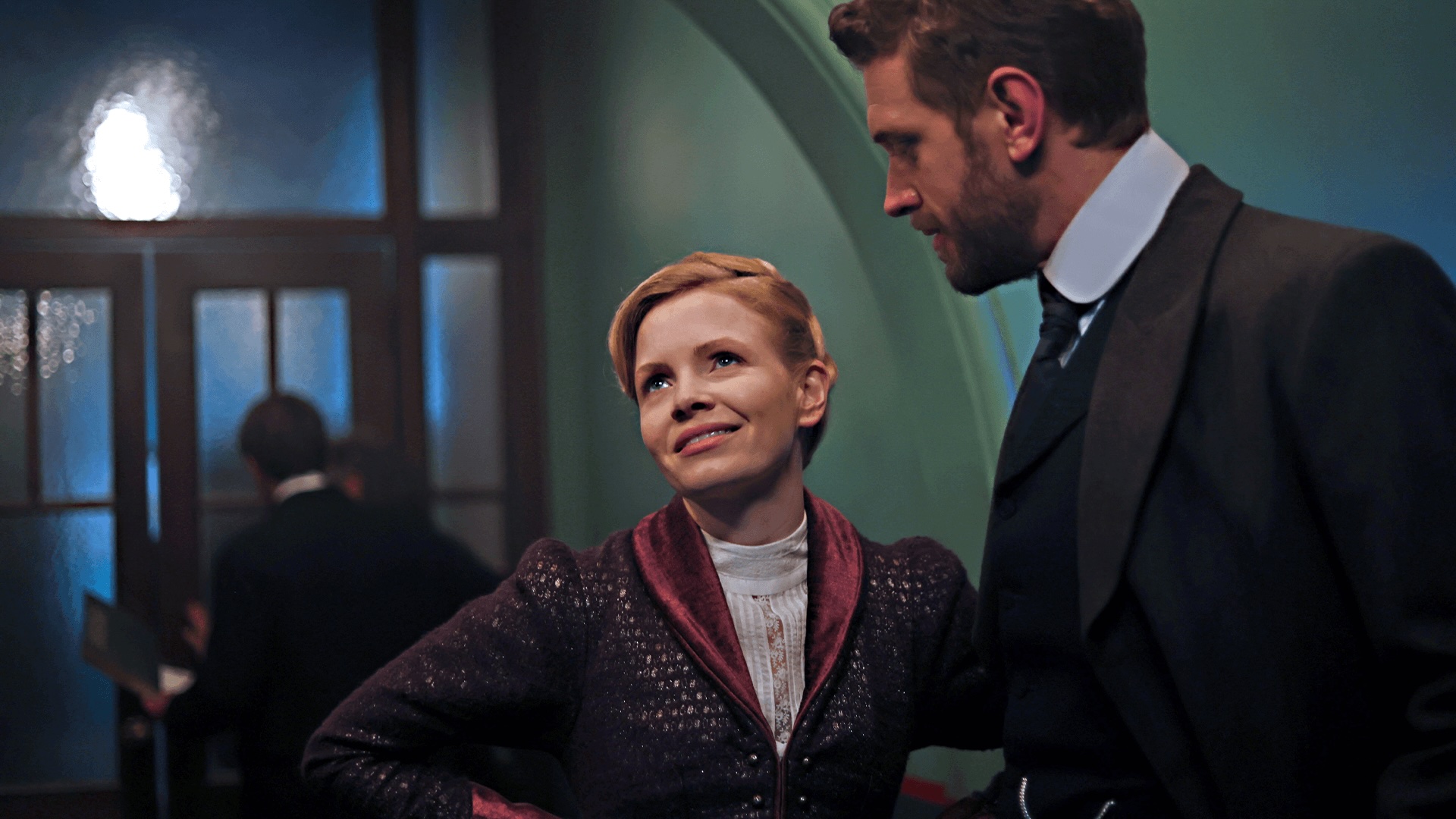 A color image from the set of Miss Scarlet Season 6 showing actor Kate Phillips in costume as Eliza Scarlet next to actor Tom Durant-Pritchard as DI Alexander Blake. The period mystery series airs on MASTERPIECE on PBS.