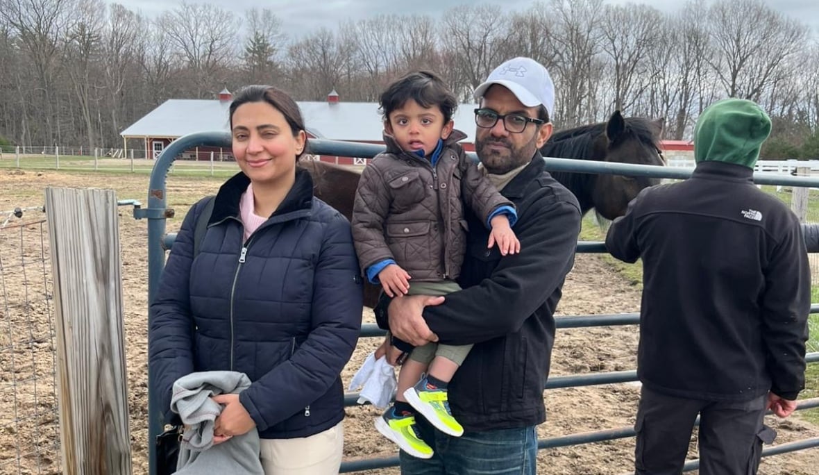 A family smiles outside an animal pen at a farm. 