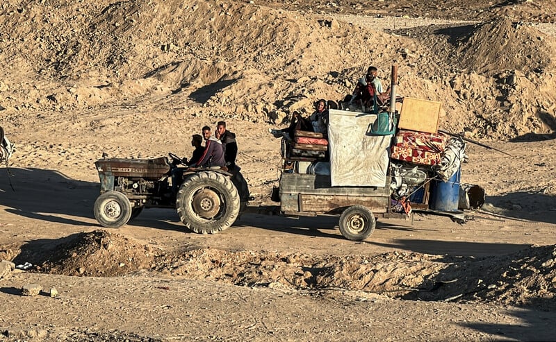 A tractor carries people and belongings along a sandy path