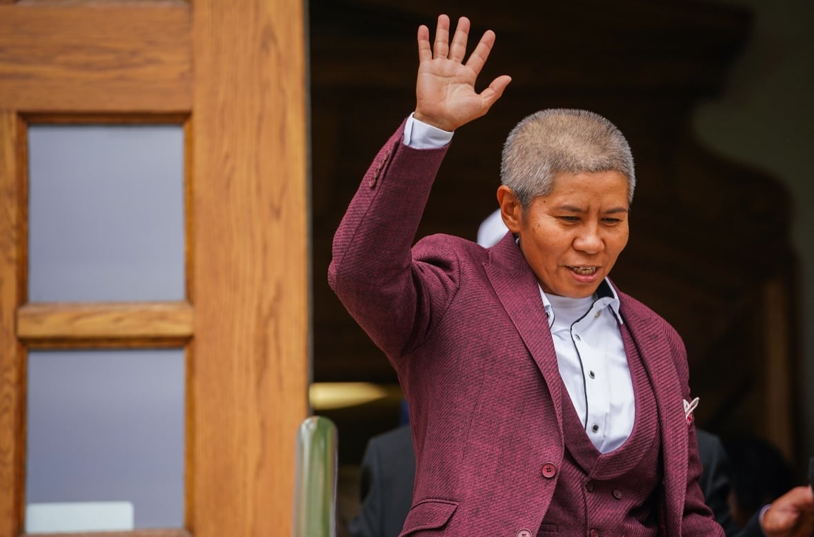 A person in a purple suit leaves a building and waves.