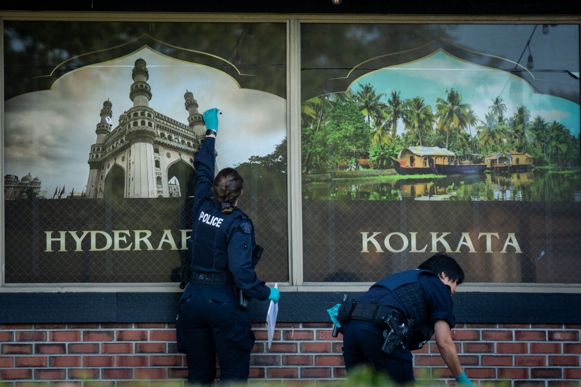 police gather evidence around a noticeable bullet hole at an Indian restaurant 