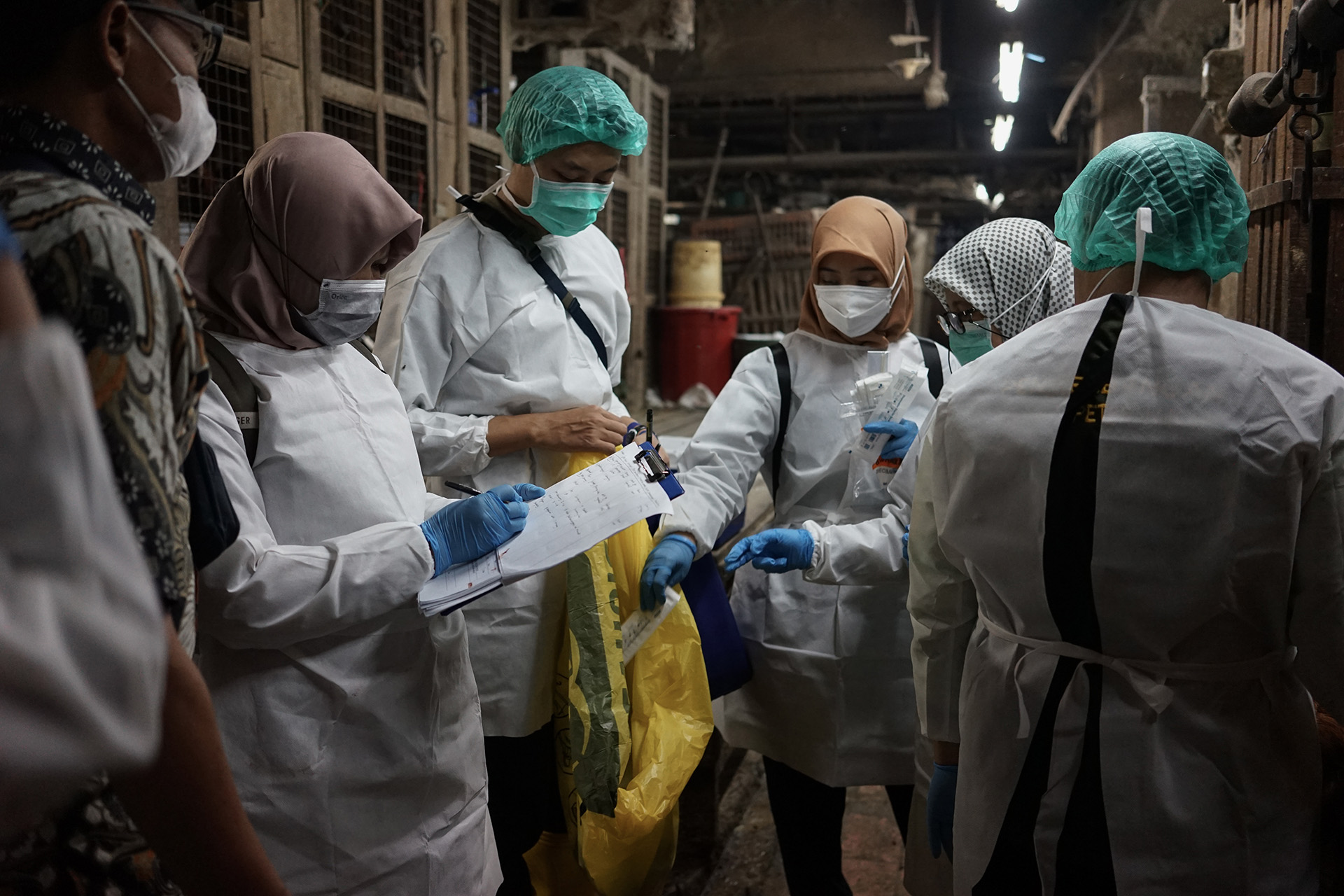 Group of people in protective gear conducting inspection and recording notes inside a dimly lit livestock facility.