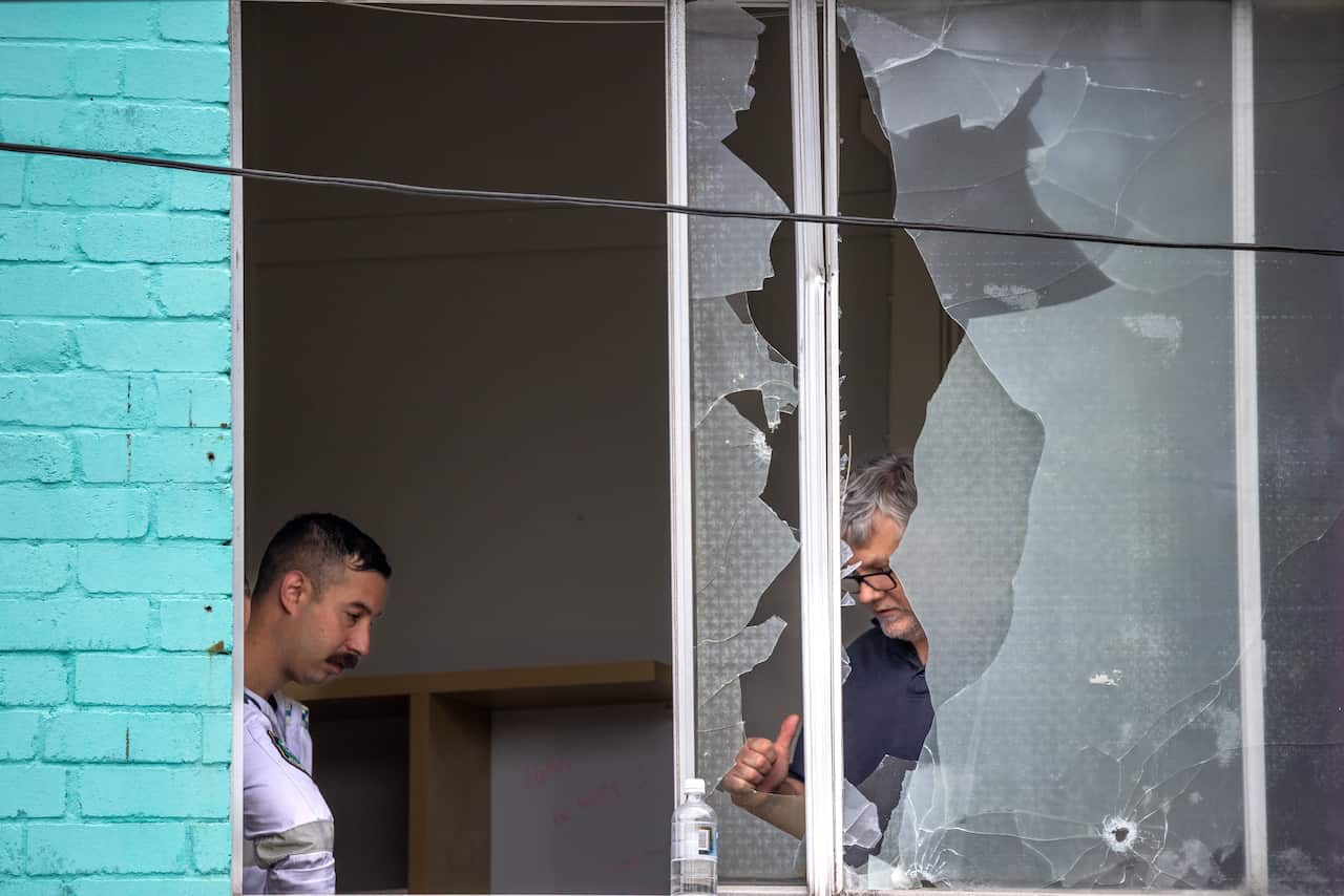 Two men standing in a room of a building with extensive damage to its window.