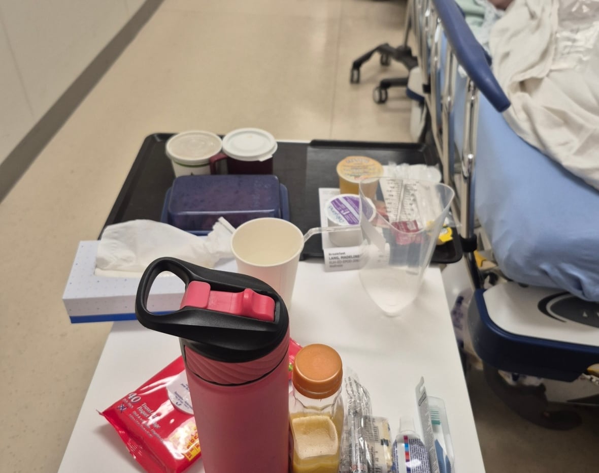A meal tray beside a hospital bed in a crowded hallway.