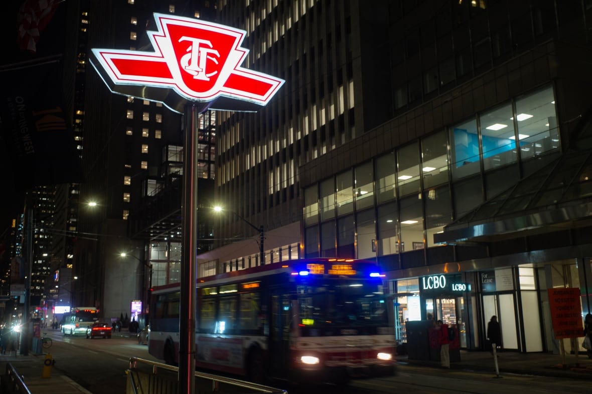 A bright TTC sign is seen near a moving bus at nighttime.